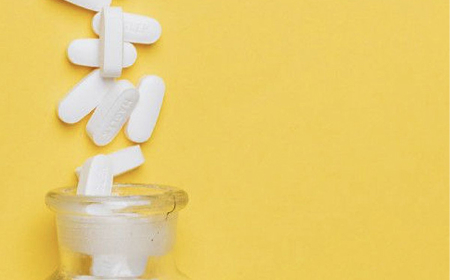 Белые таблетки падают в стеклянную банку на желтом фоне